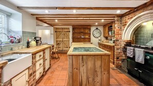 A rustic kitchen with wooden beams, a central island, a brick wall, and a vintage stove. - 3 bedroom accommodation in Sutton Benger, near Lacock (Sutton Benger, near Lacock)