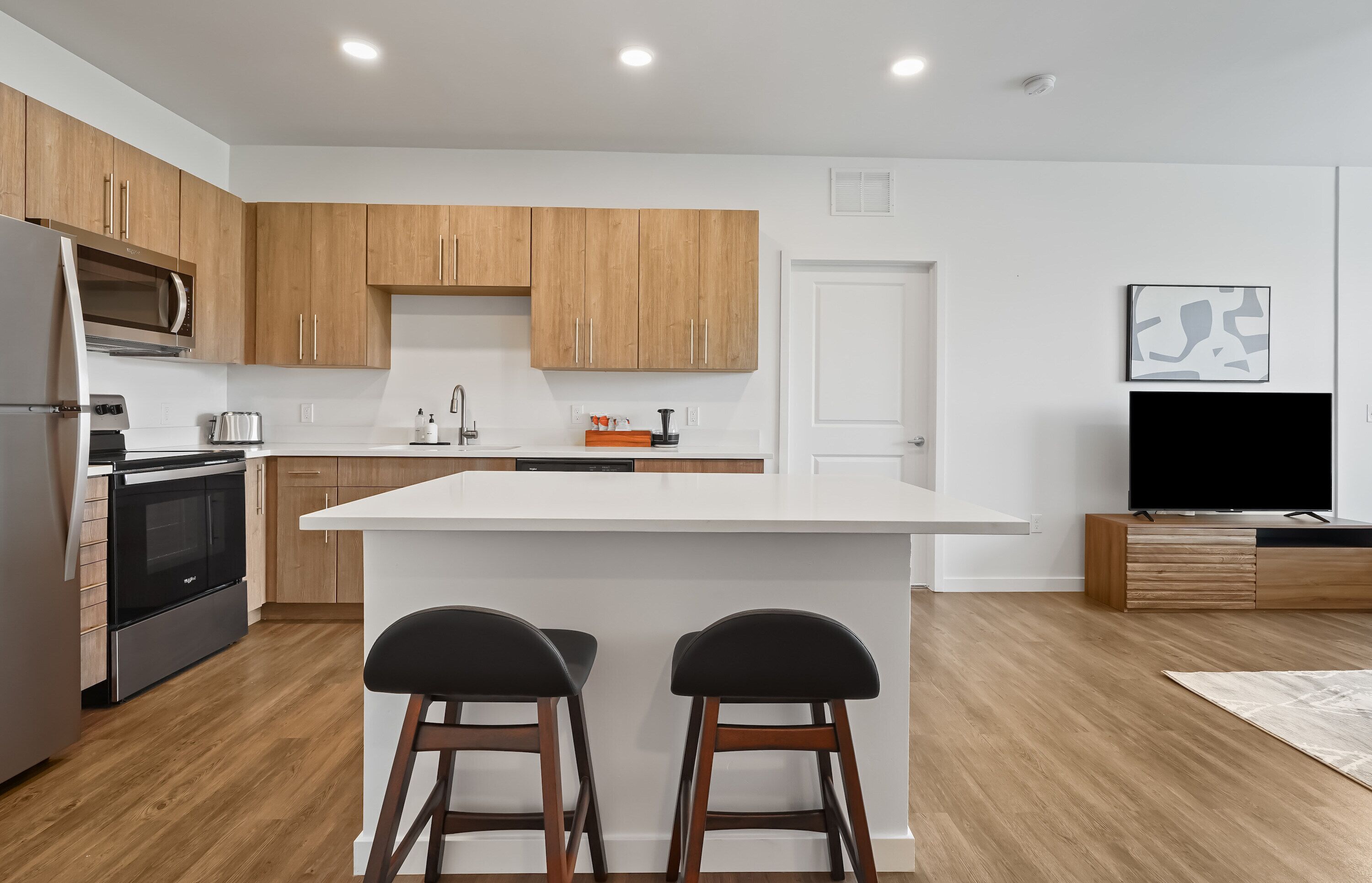 A modern kitchen with wooden cabinets, a white countertop, and a built-in island with two stools.