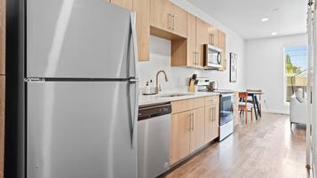 A modern kitchen with a white refrigerator, wooden cabinets, a dishwasher, and a microwave.