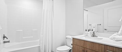 Een moderne badkamer met een badkuip, toilet en een houten wastafelmeubel.