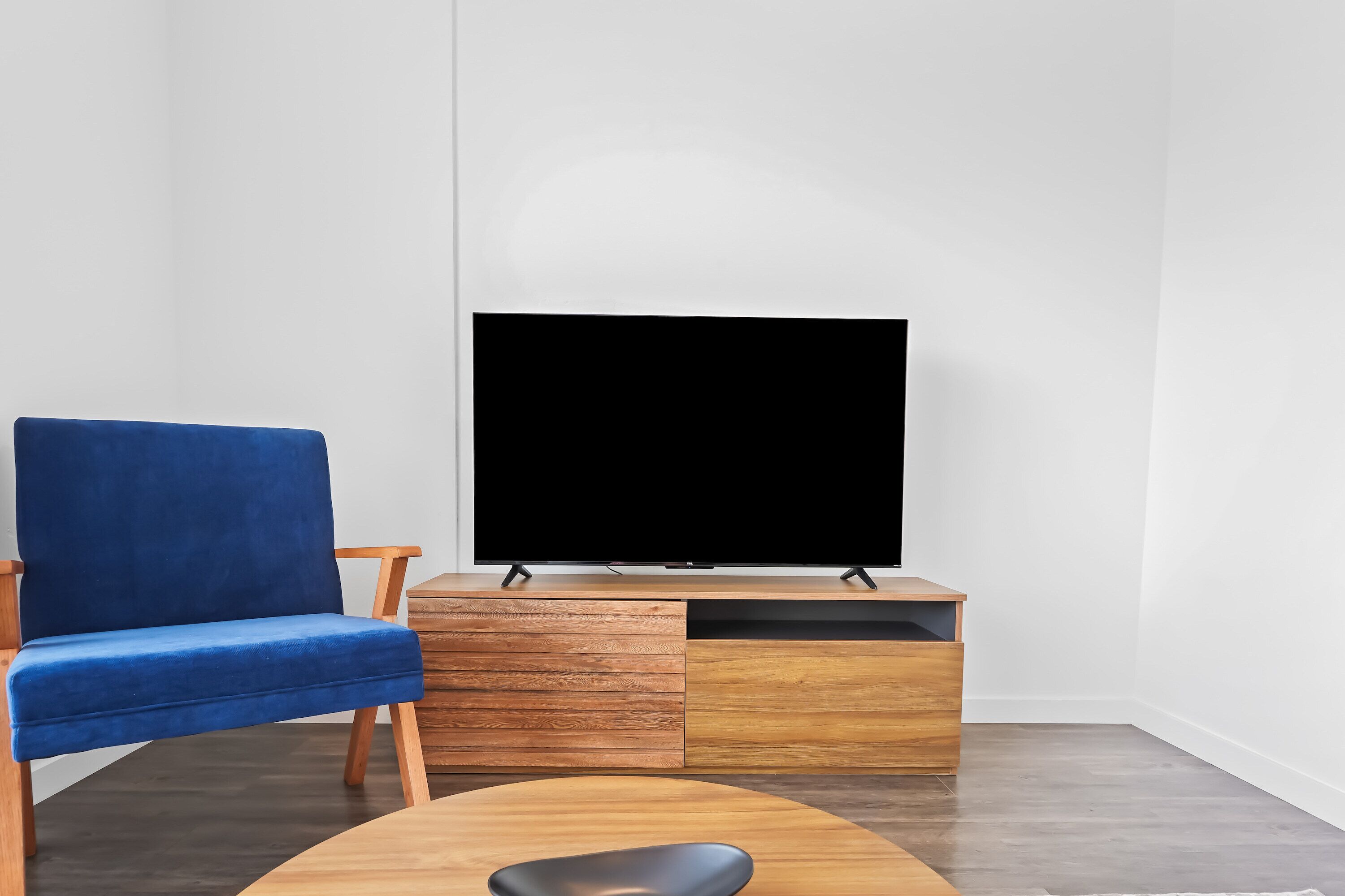 Una sala de estar moderna con un sillón azul, un mueble de entretenimiento de madera y un televisor de pantalla plana grande.