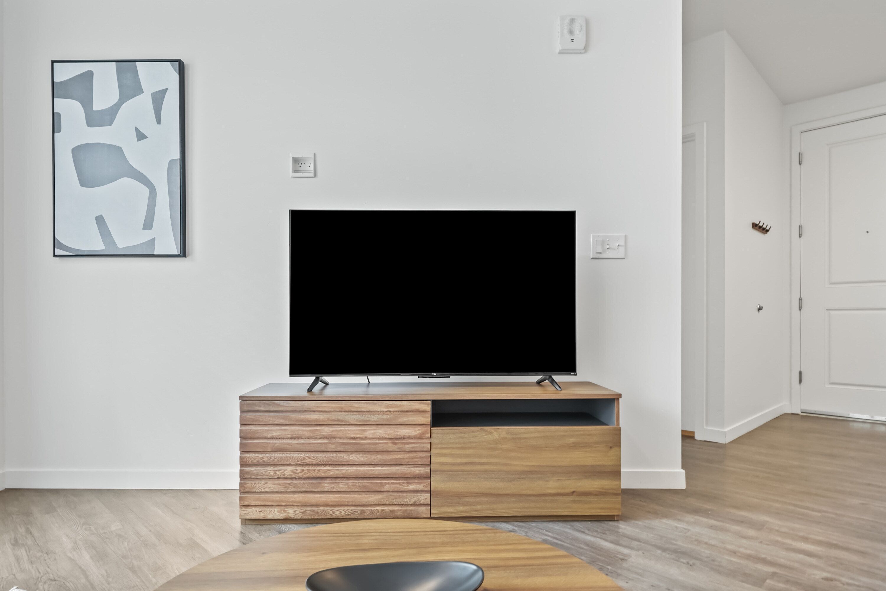 A modern living room with a flat-screen TV on a wooden TV stand, a coffee table, and a framed abstract art piece on the wall.