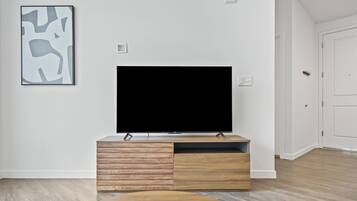 A modern living room with a flat-screen TV on a wooden TV stand, a coffee table, and a framed abstract art piece on the wall.