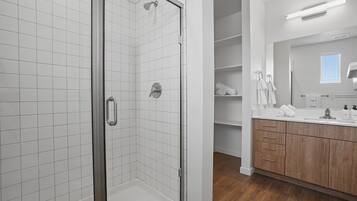 A modern bathroom with a glass-enclosed shower, white tiled walls, wooden cabinets, and a large mirror.