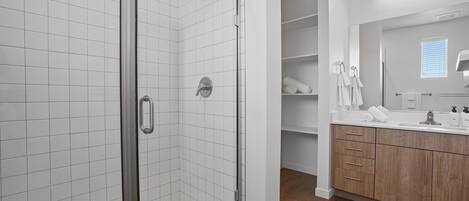 A modern bathroom with a glass-enclosed shower, white tiled walls, wooden cabinets, and a large mirror.