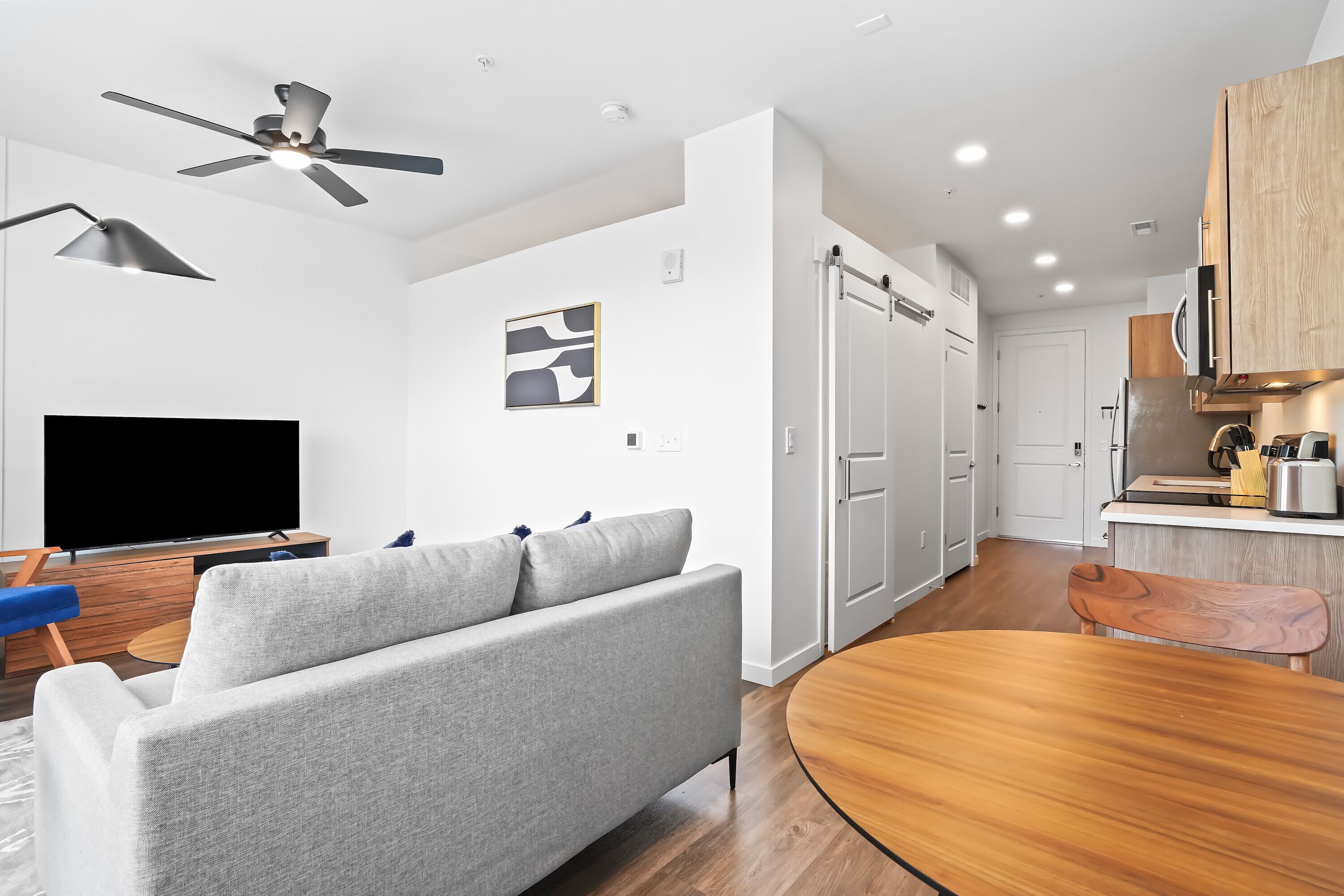 A modern living room with a grey sofa, wooden dining table, and a TV.