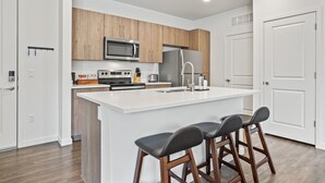 A modern kitchen with wooden cabinets, a stainless steel refrigerator, a microwave, and a large island with bar stools. - Kasa on the River Boise (Boise)