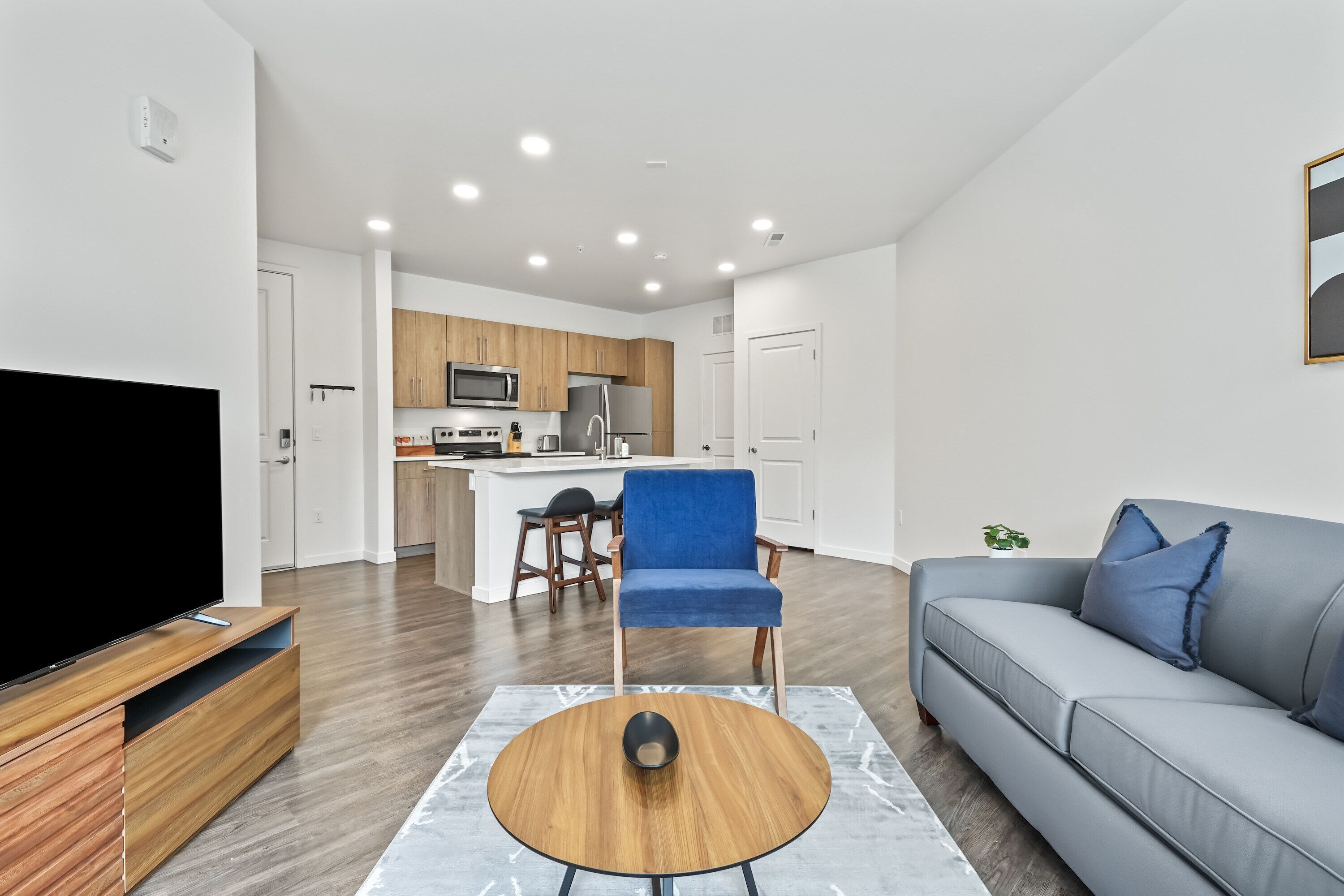 A modern living room with a flat-screen TV, a blue chair, a grey sofa, and a wooden coffee table.