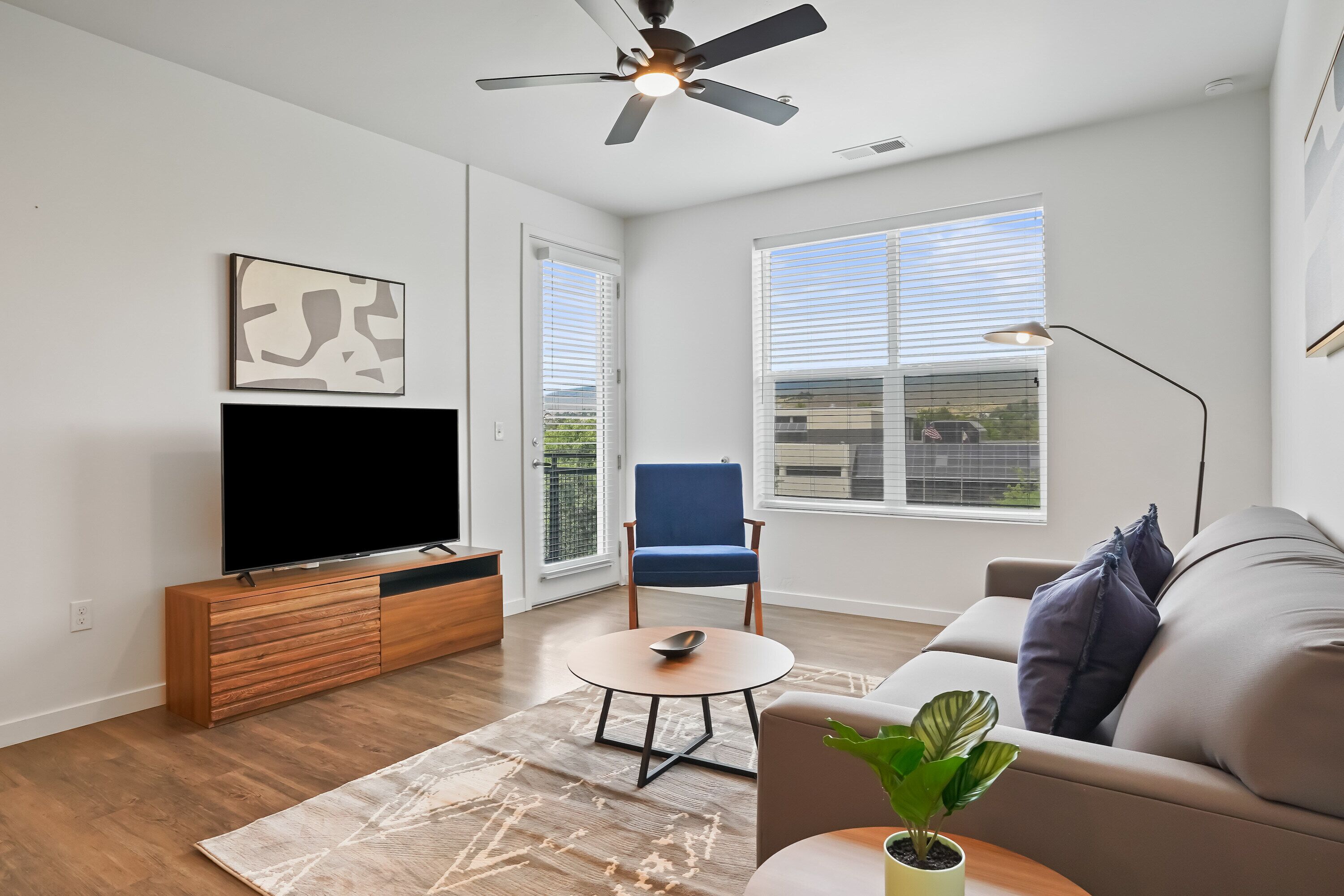 A modern living room with a flat-screen TV, a blue chair, a sofa, a coffee table, and a ceiling fan.