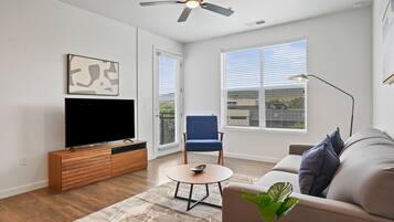 A modern living room with a flat-screen TV, a blue chair, a sofa, a coffee table, and a ceiling fan.