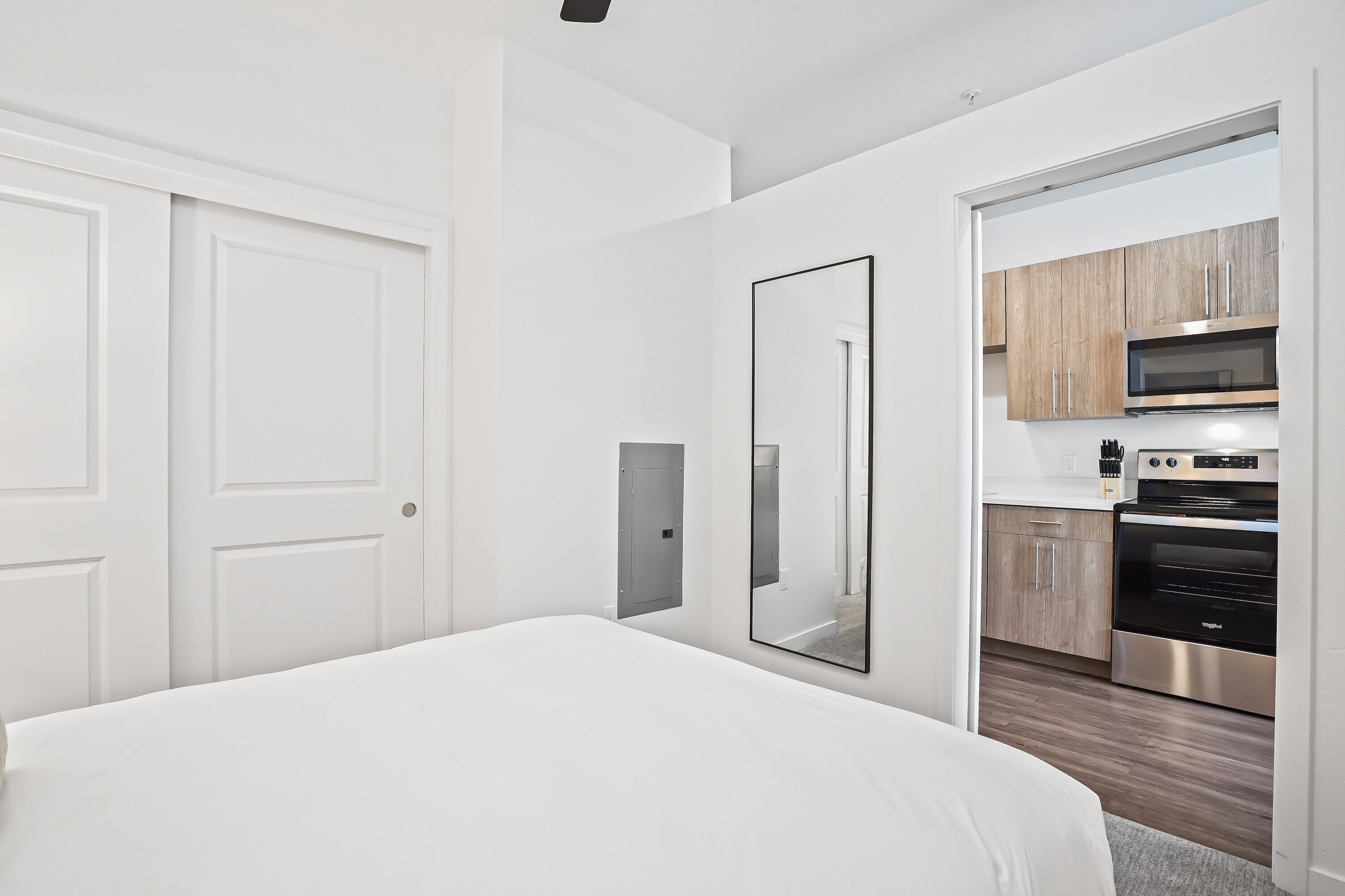 Ett modernt hotellrum med en stor säng, en inbyggd garderob, en spegel och ett litet kök med mikrovågsugn och ugn.