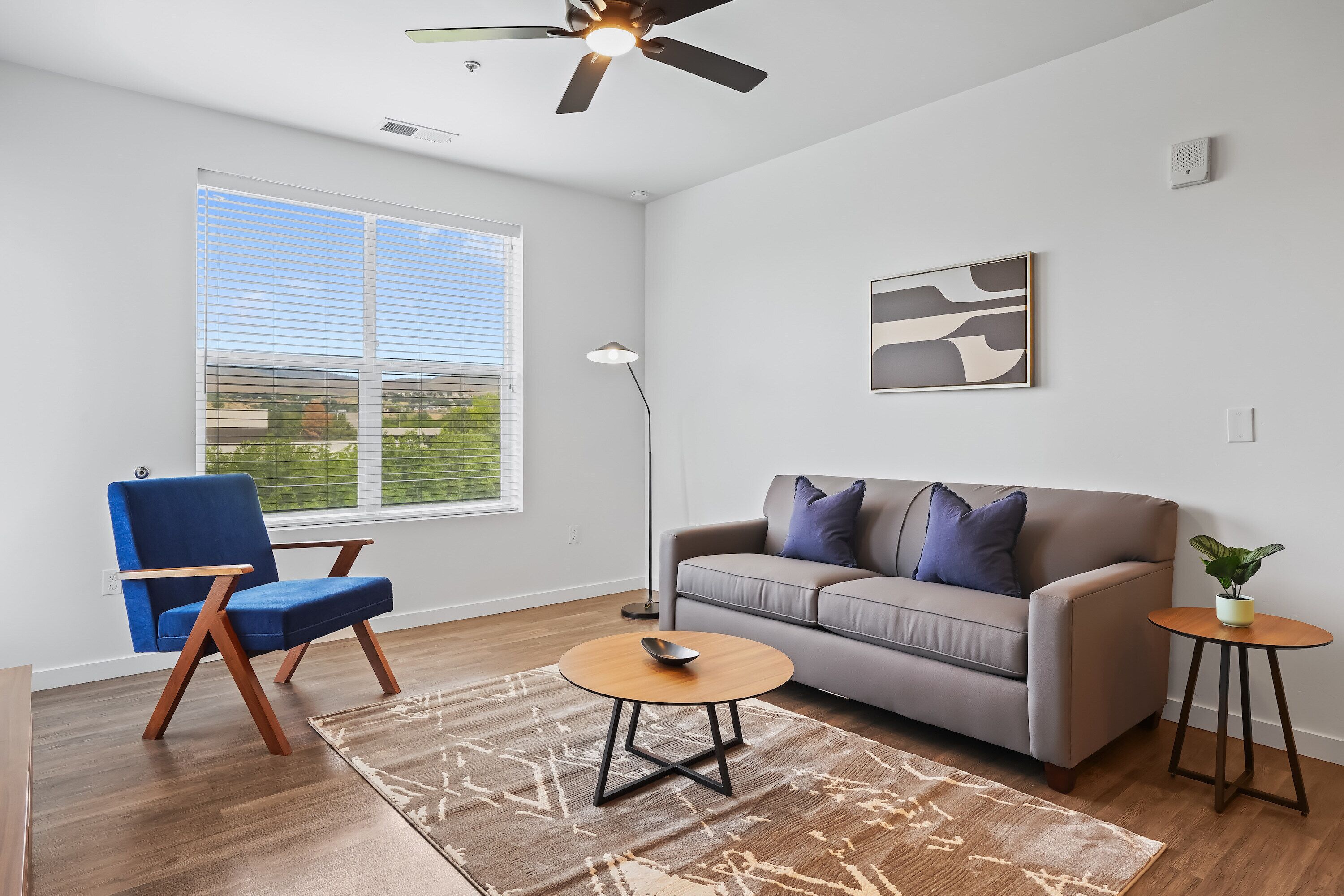 A modern living room with a blue chair, grey sofa, and a small round table.
