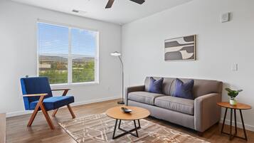 A modern living room with a blue chair, grey sofa, and a small round table.