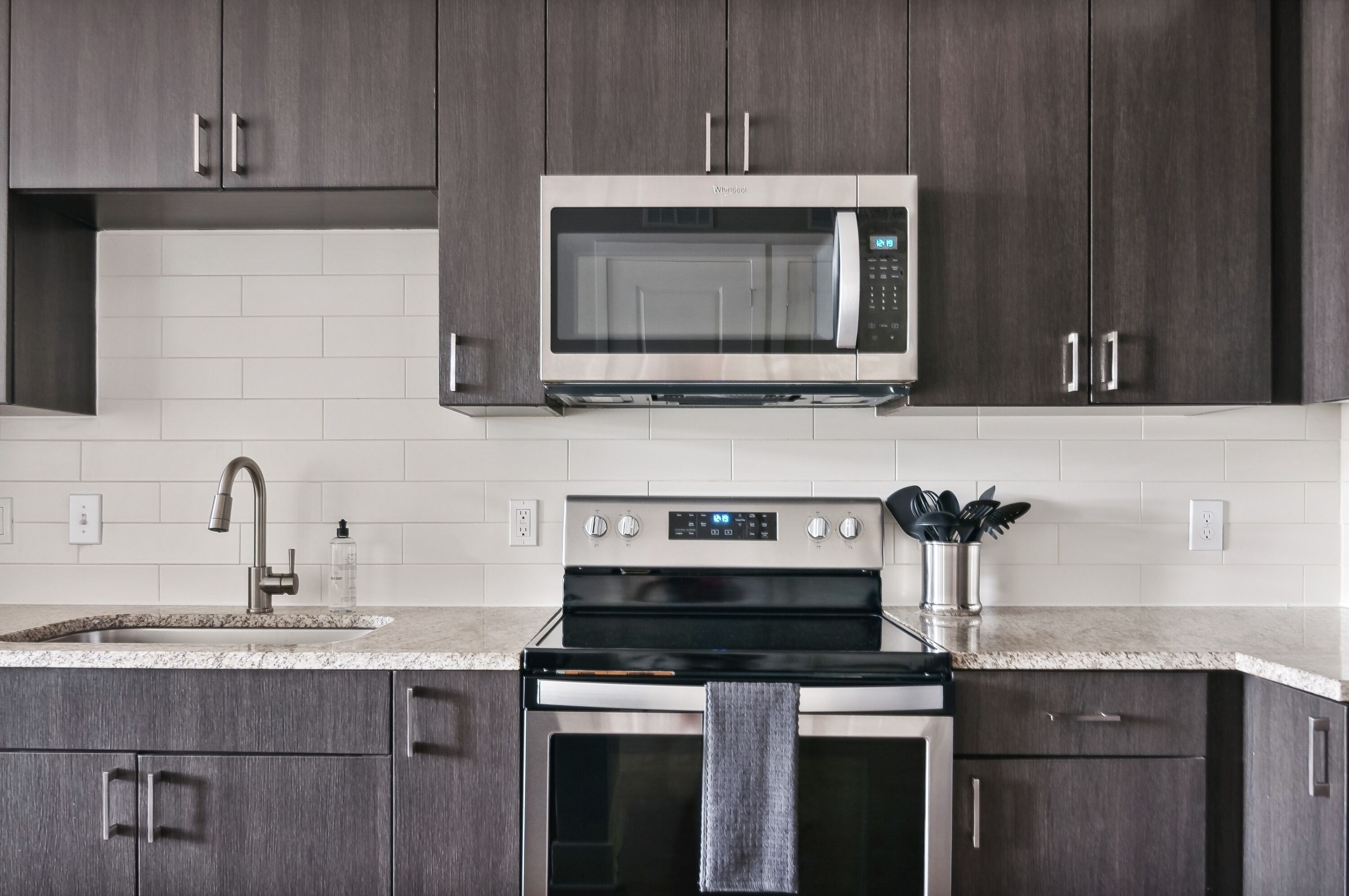 A modern kitchen with dark wood cabinets, a stainless steel microwave, a built-in oven, and a granite countertop.
