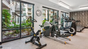 Un gimnasio moderno con máquinas de cardio, un reloj y amplias ventanas con vistas a una zona residencial.