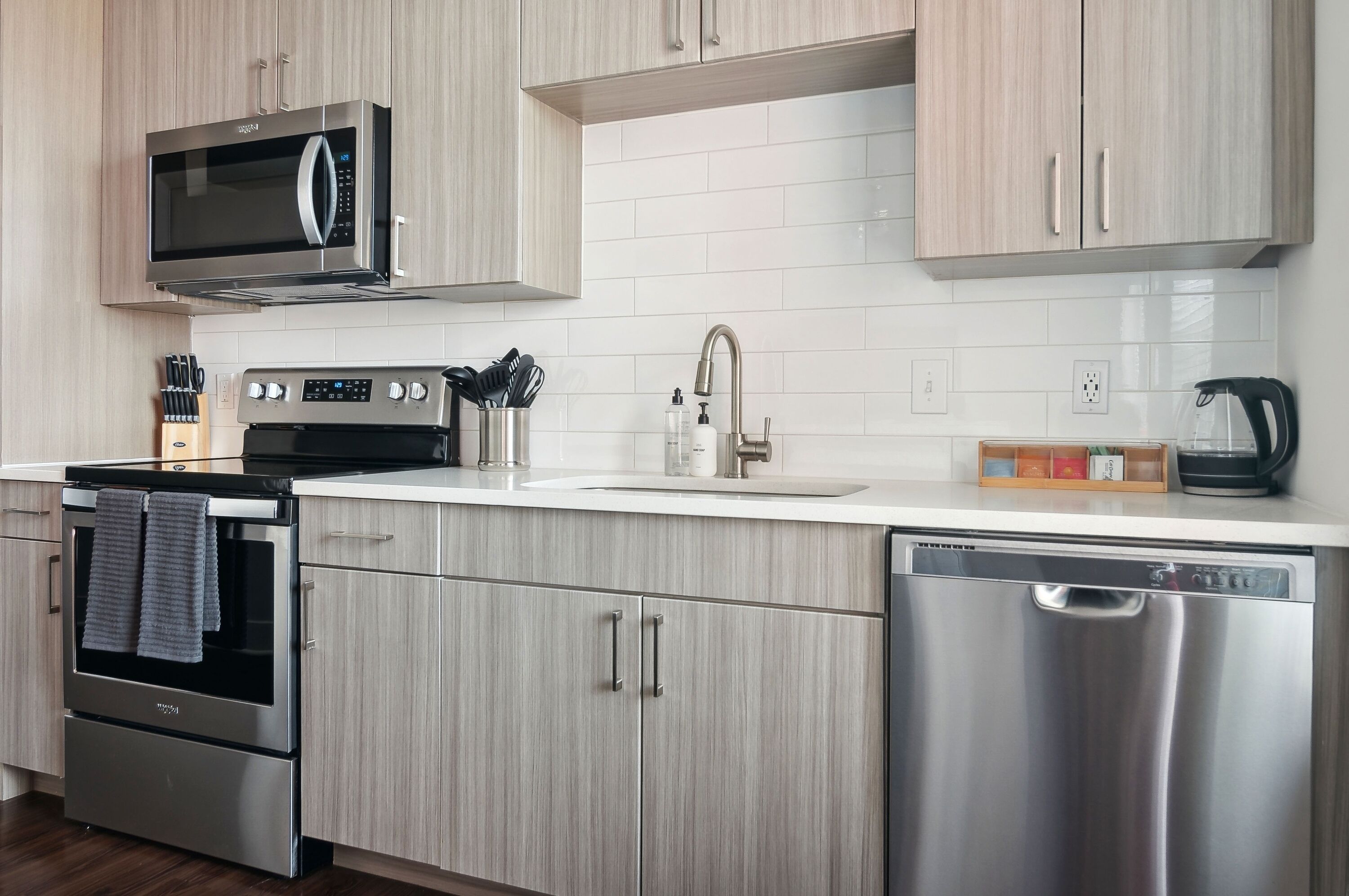 A modern kitchen with stainless steel appliances, light wood cabinets, and a white countertop.