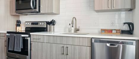 A modern kitchen with stainless steel appliances, light wood cabinets, and a white countertop.