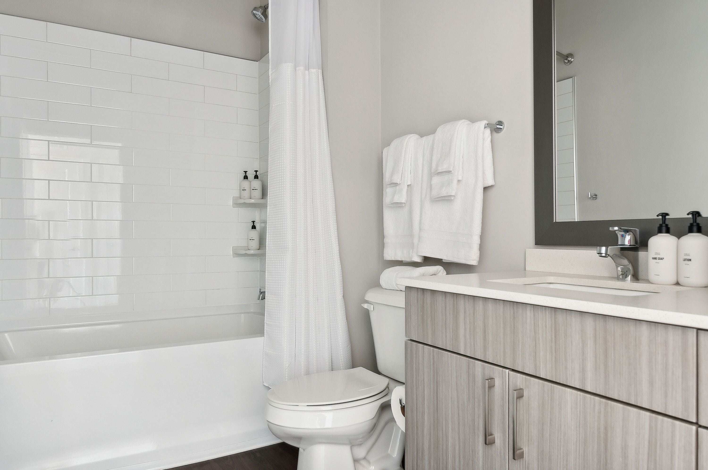 A modern bathroom with a white toilet, a bathtub, a shower curtain, a vanity with a mirror, and toiletries on the counter.