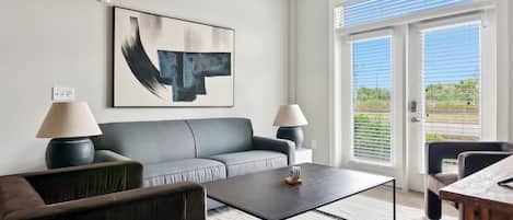 A modern living room with a grey sofa, two side tables with lamps, a coffee table, and a large abstract painting on the wall.