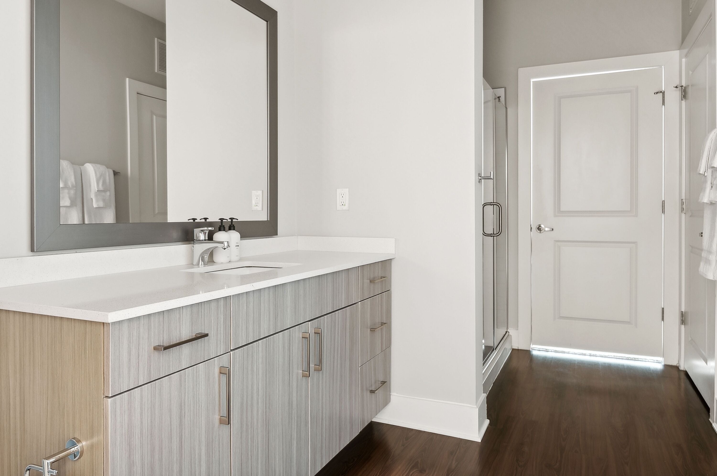 Une salle de bain moderne avec un grand miroir, un meuble-lavabo blanc et des armoires en bois.