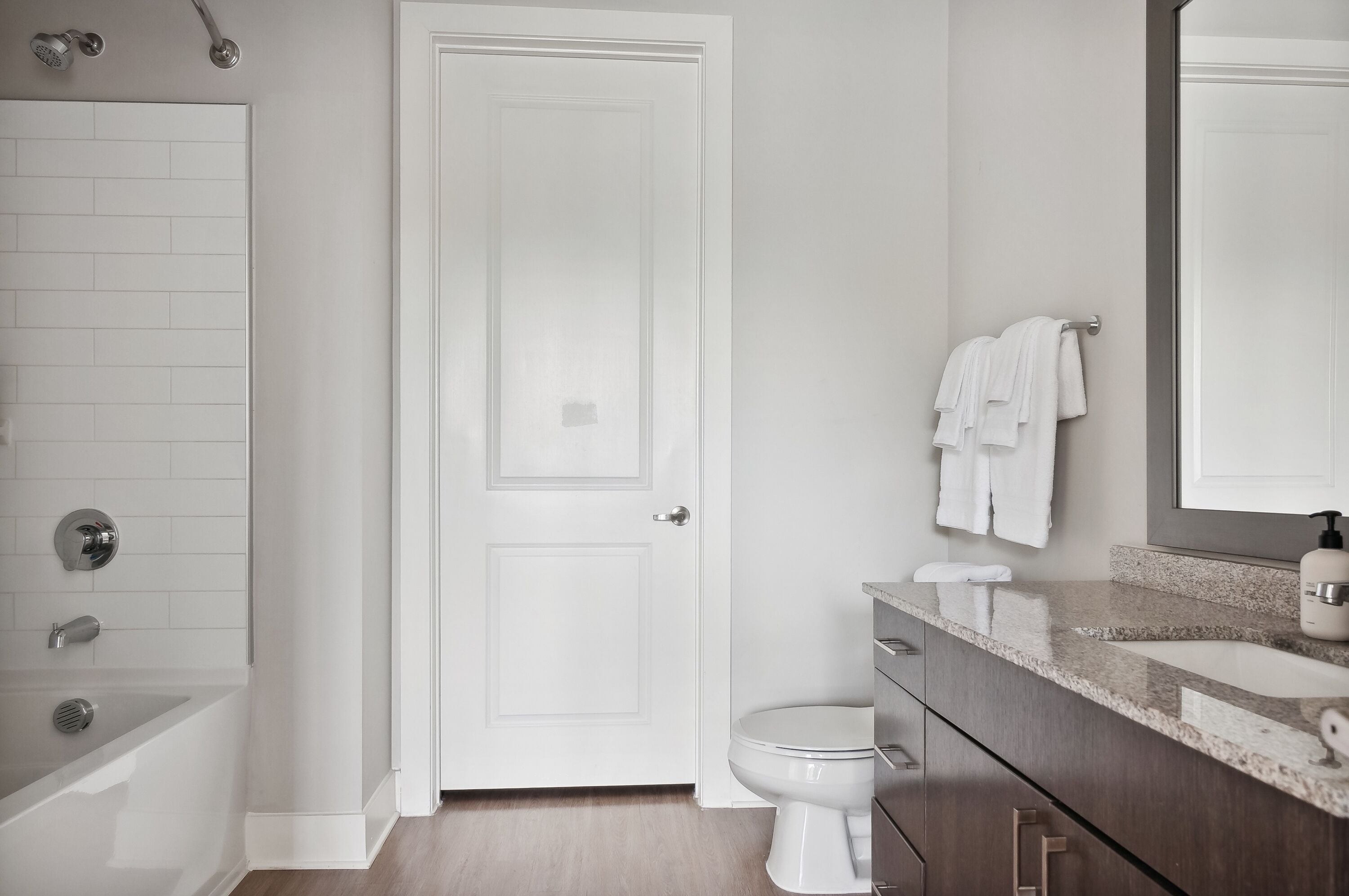 Une salle de bain moderne avec une porte blanche, une baignoire, des toilettes et un meuble-lavabo avec un miroir.