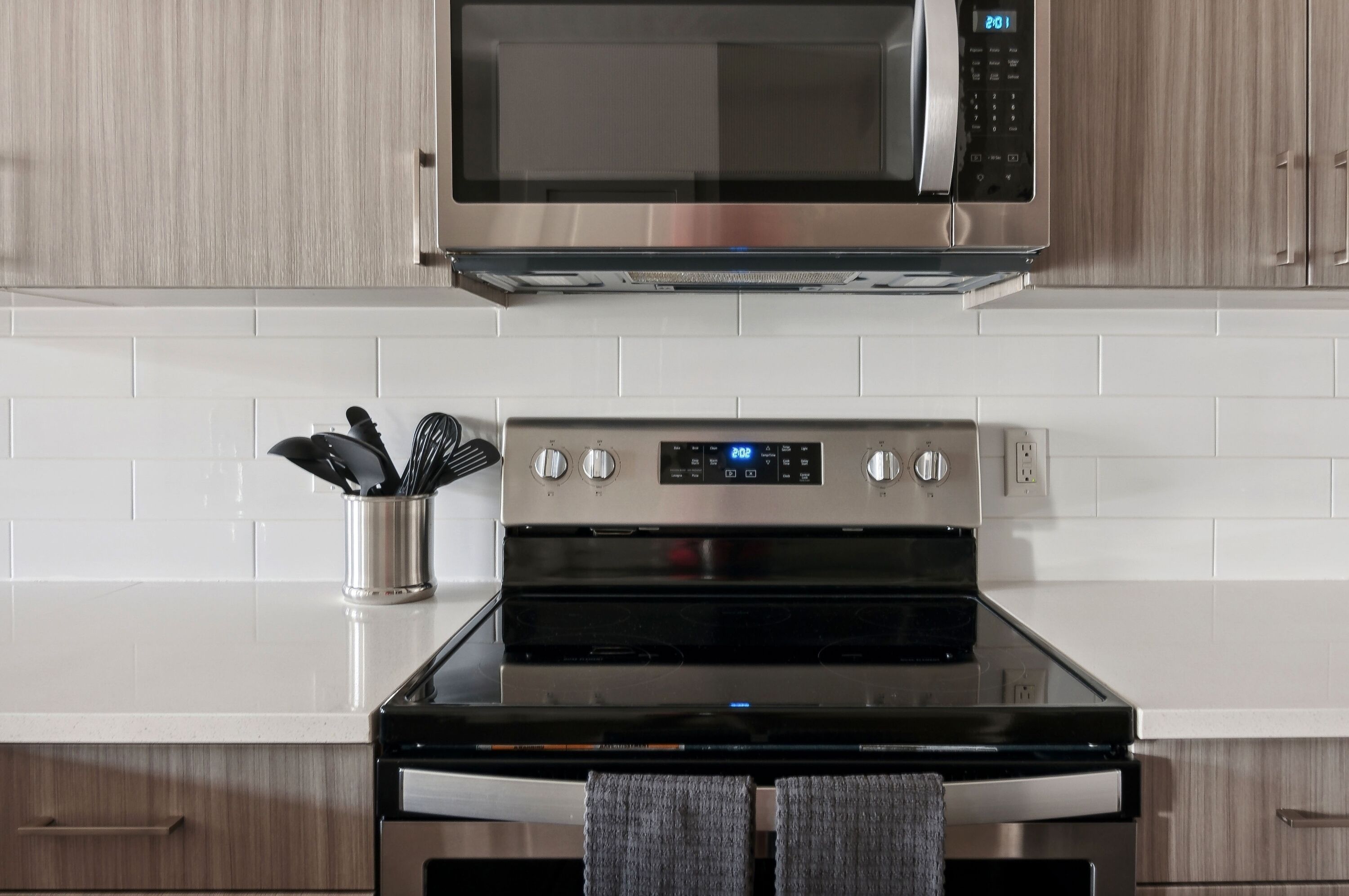 A kitchen with a stainless steel microwave, oven, and a set of knives in a container.
