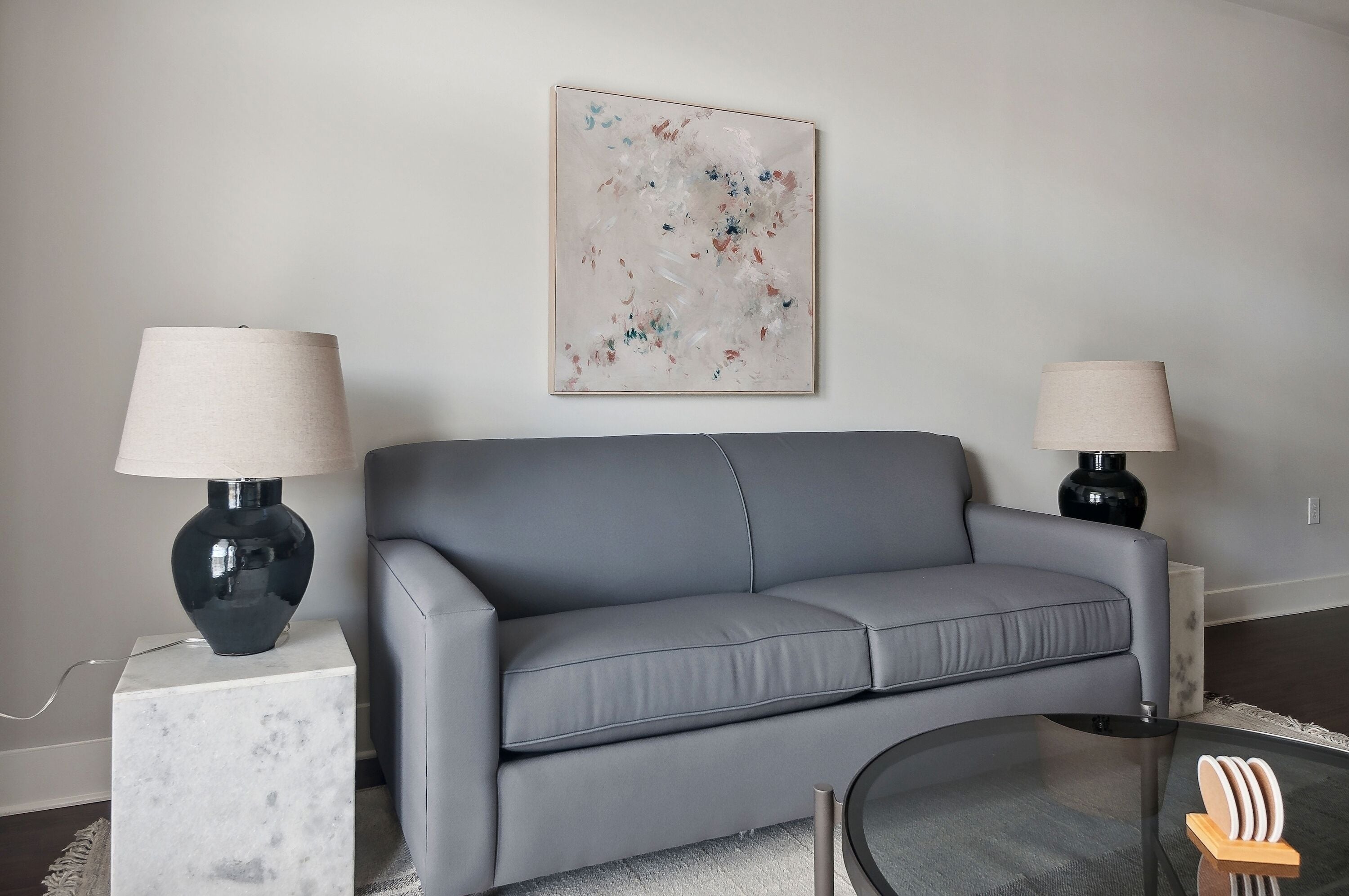 Una sala de estar moderna con un sofá gris, dos lámparas negras, una mesita auxiliar de mármol y una mesa de centro de vidrio.