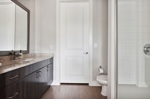 Une salle de bain avec un meuble-lavabo en bois foncé, une porte blanche, des toilettes et une cabine de douche en verre.