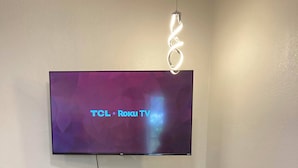A flat-screen TV mounted on a wall above a wooden dining table with two stools.