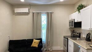 A compact kitchen with a black sofa, a microwave, a sink, and a window with curtains.