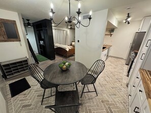 A dining area with a round table, four chairs, a chandelier, and a kitchen in the background. - The Cozy Getaway  (Colorado Springs)