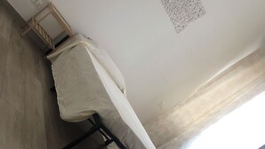 Un dormitori amb un llit, terres de fusta, una finestra amb cortines i una làmpada penjada a la paret.