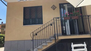 Un edifici amb façana beix, una escala amb baranes negres i una finestra amb reixatge decoratiu.