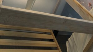 Habitació amb llit, panell de capçal de fusta i una làmpada penjada a la paret.