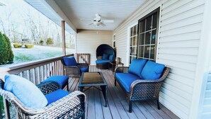 Eine überdachte Veranda mit Korbmöbeln, einem Deckenventilator und Blick auf den Garten.