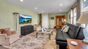Una sala de estar con un sofá, una mesa de centro y un televisor. Se ve una escalera que conduce a otra habitación.