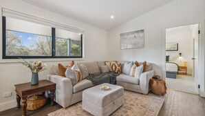 A living room with a large window, a sofa, a coffee table, and a painting on the wall. - Nowhere Cottage rural retreat (Crackenback)