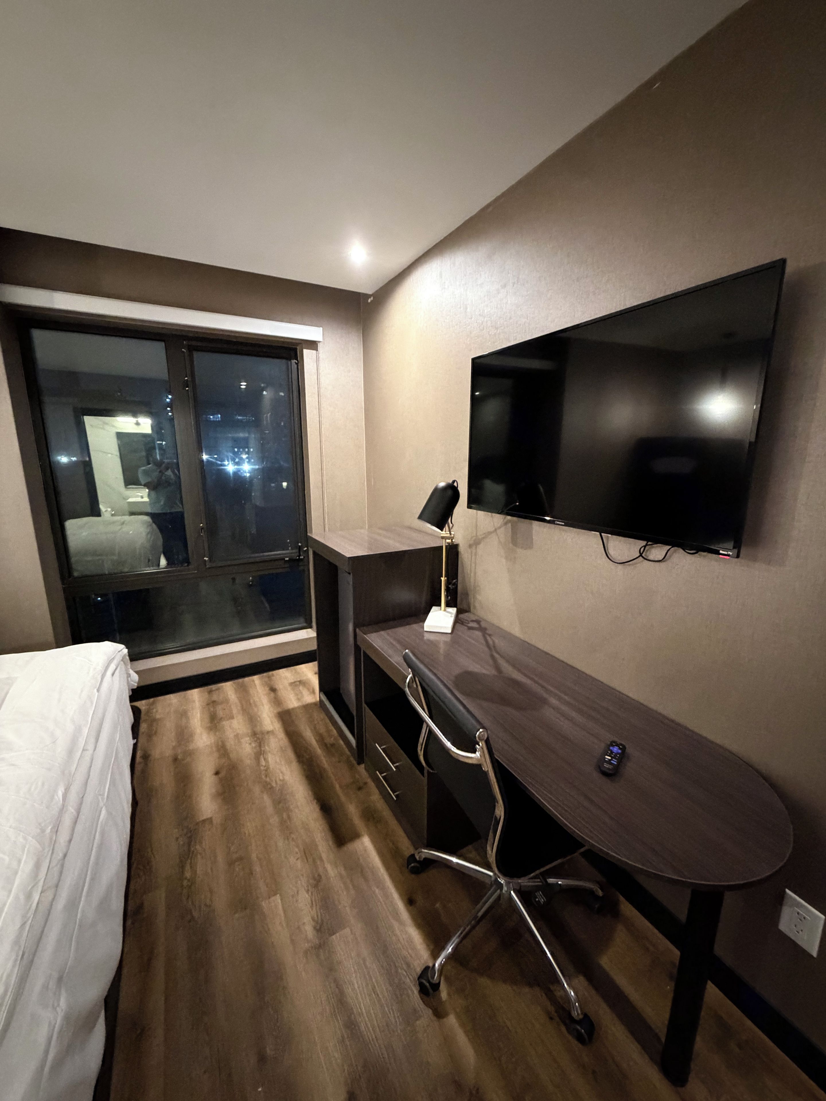 Un dormitorio con cama, escritorio, silla, televisor y ventana.