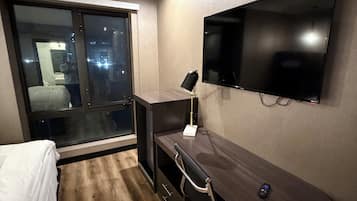 Un dormitorio con cama, escritorio, silla, televisor y ventana.