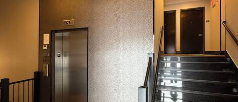 Um saguão de hotel com escadas, elevador e parede com textura.