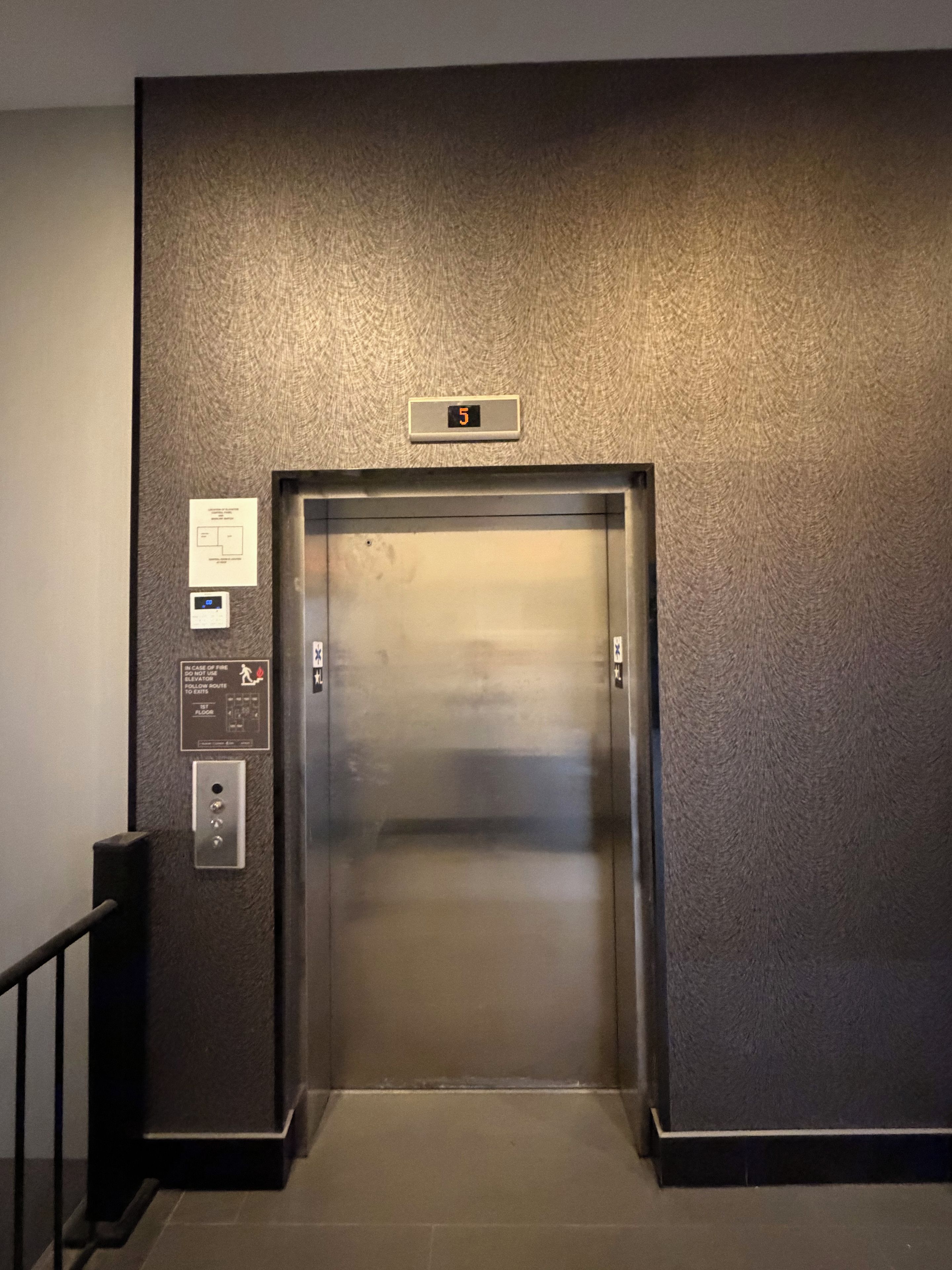 An elevator with a digital display showing the number 5, emergency instructions, and a control panel with buttons.