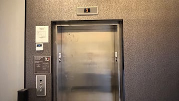 Un ascenseur doté d’un écran numérique affichant le chiffre 5, des instructions de sécurité et un panneau de commande avec des boutons.