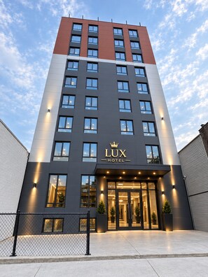 A modern hotel building with a prominent entrance, multiple floors, and a clear sky. - LUX HOTEL (Long Island City)