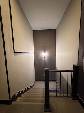 A staircase with a handrail, a light fixture on the wall, and a door at the top. - LUX HOTEL (Long Island City)