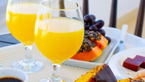 Two glasses of orange juice on a table with a plate of food including a fruit salad and a chocolate dessert.