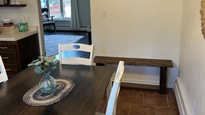 A dining area with a dark wooden table, white chairs, and a bench. A decorative wall sign with the word "Eat" is visible. - Close to Everything! Freshly updated ranch home. (Shawano)