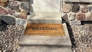 A house entrance with a stone foundation, a white door with a glass panel, and a 'WELCOME' mat. - Close to Everything! Freshly updated ranch home. (Shawano)