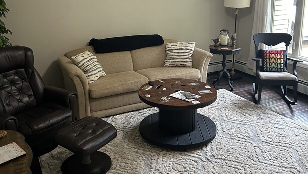 A living room with a beige sofa, a black leather armchair, a coffee table, and a ceiling fan. The word "SHAWANO" is displayed on the wall. - Close to Everything! Freshly updated ranch home. (Shawano)