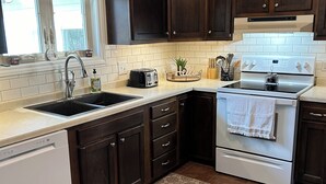 A kitchen with dark wooden cabinets, a white dishwasher, a white stove, and a window above the sink. - Close to Everything! Freshly updated ranch home. (Shawano)