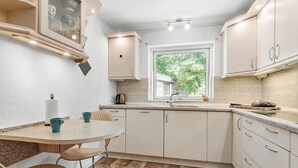Una cocina compacta con una mesa redonda, una ventana con vistas a la vegetación y armarios de colores claros.